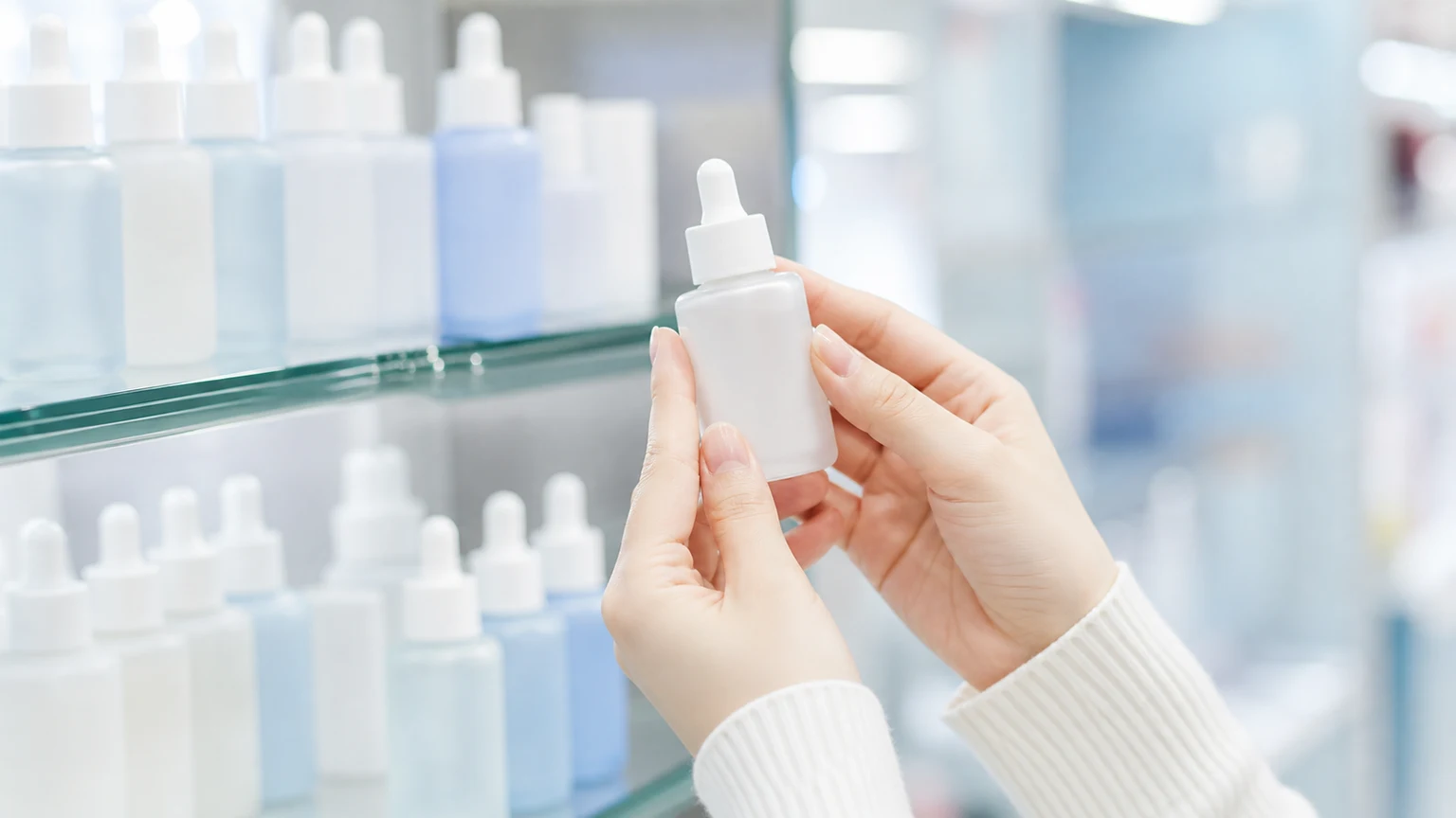 スキンケアの棚から美容液のボトルを1本だけ取り出し、表側を見ている手元