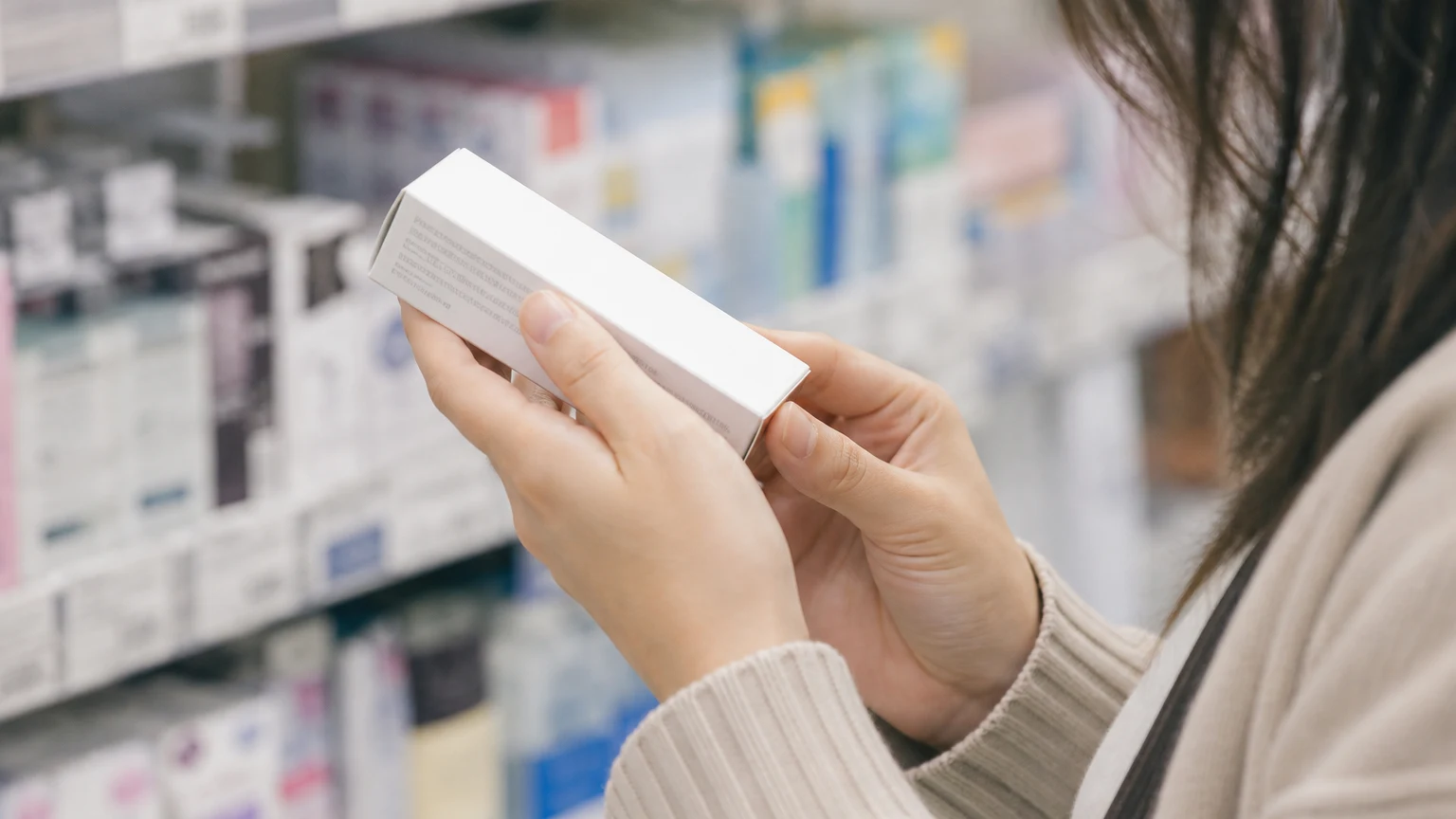 薬の棚の前で、クリームの箱の側面にある効能・効果の欄を読んでいる手元