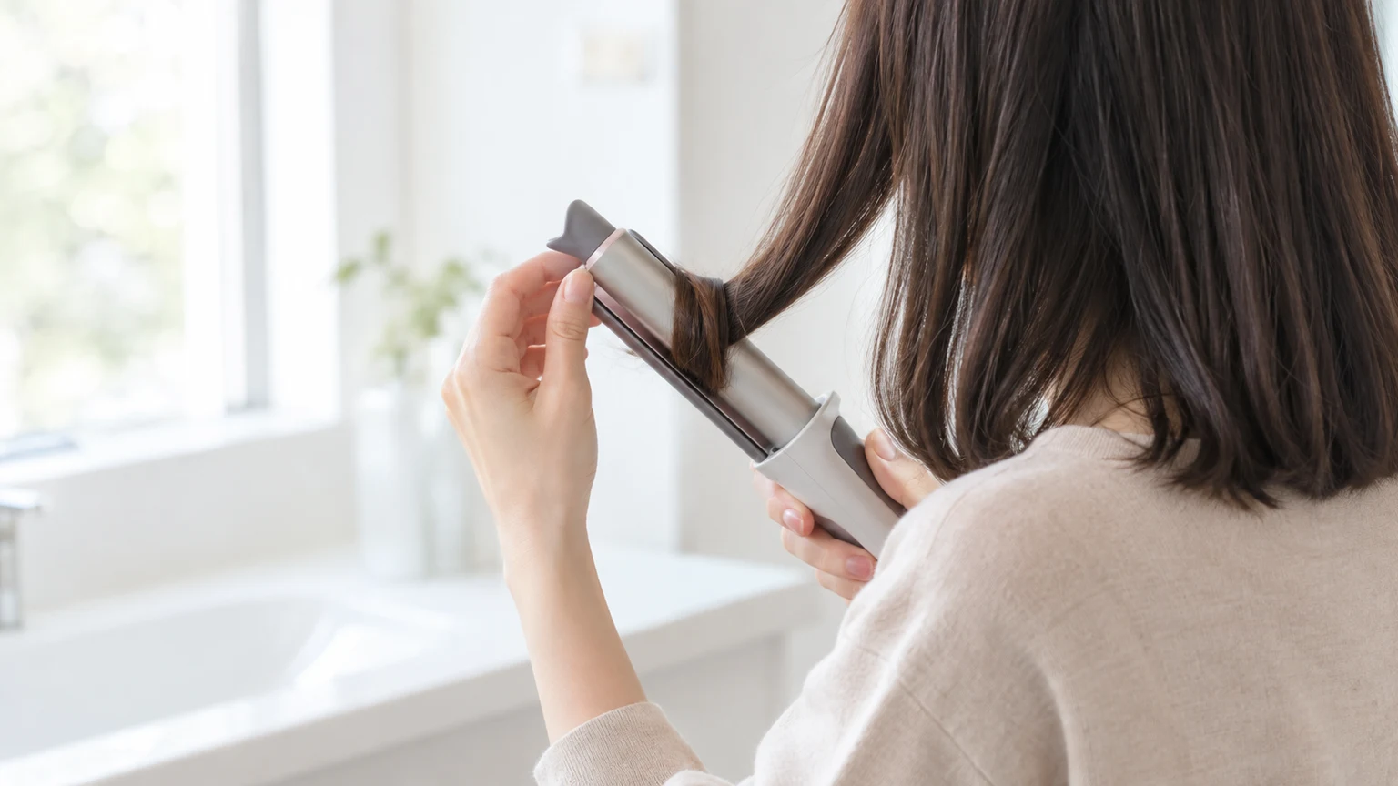 洗面台の前で、2WAYのヘアアイロンの丸い面に毛束を巻きつけている手元