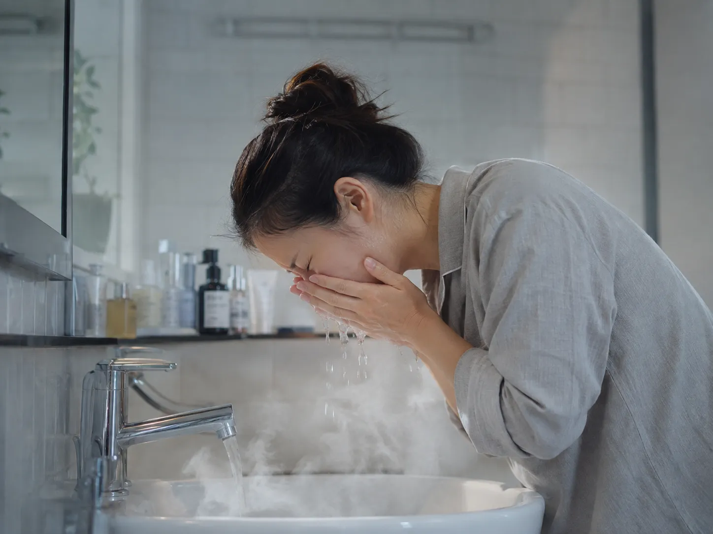 湯気の立つ熱いお湯で洗顔する様子