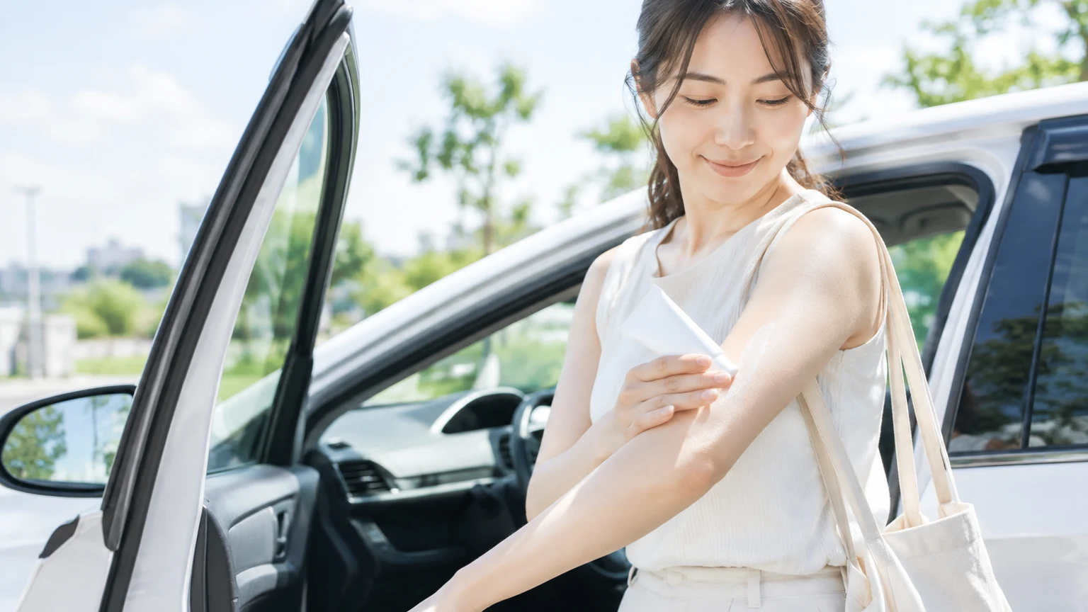 駐車場で、車に乗る前に右腕へ日焼け止めを塗っているところ
