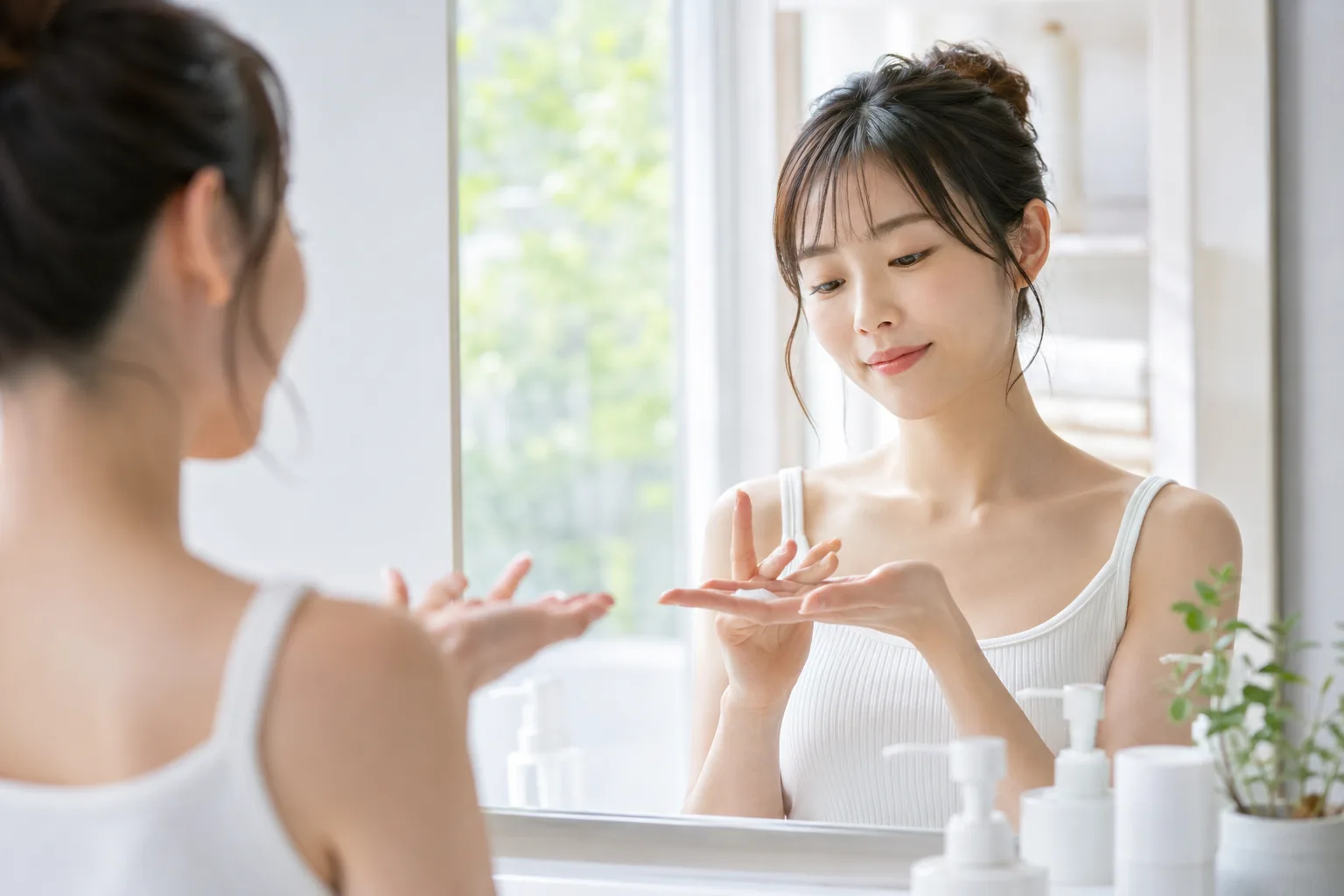 洗面所で鏡を見ながら手のひらに出した日焼け止めを確認し、自分に合うタイプを見直す女性の写真