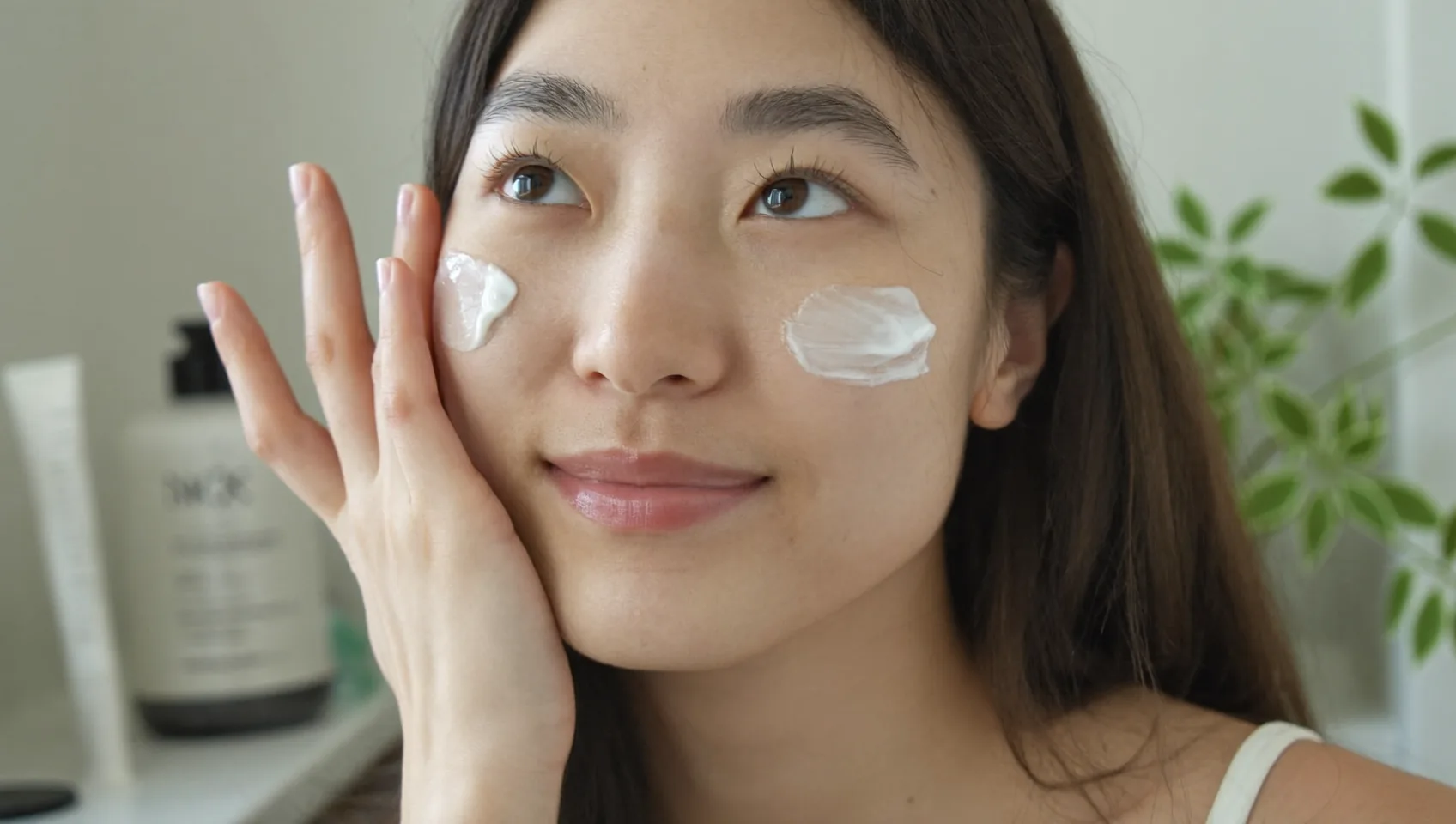 洗顔後に頬へ保湿クリームを両手の指先でなじませる女性