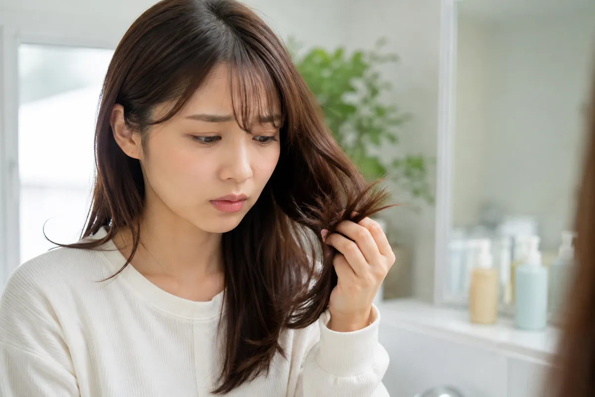 毛先を指でつまみパサつきに気づく女性