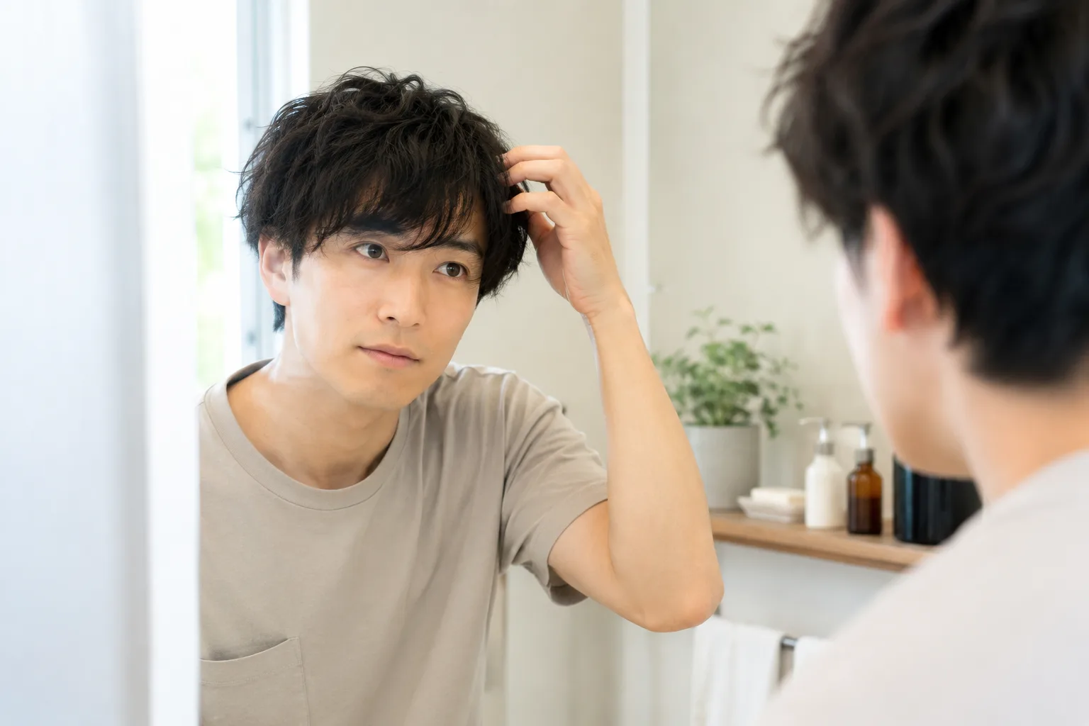 鏡の前で自分のくせ毛に触れながら見つめる男性