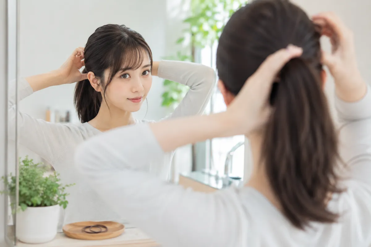 鏡の前でポニーテールを結ぶ位置を優しく調整する女性