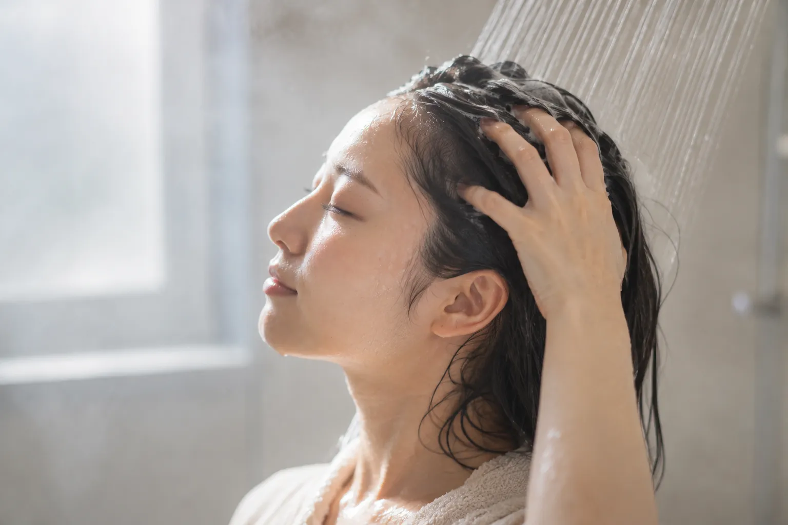 シャワーで頭皮を優しくすすぎながらシャンプーする女性の横顔
