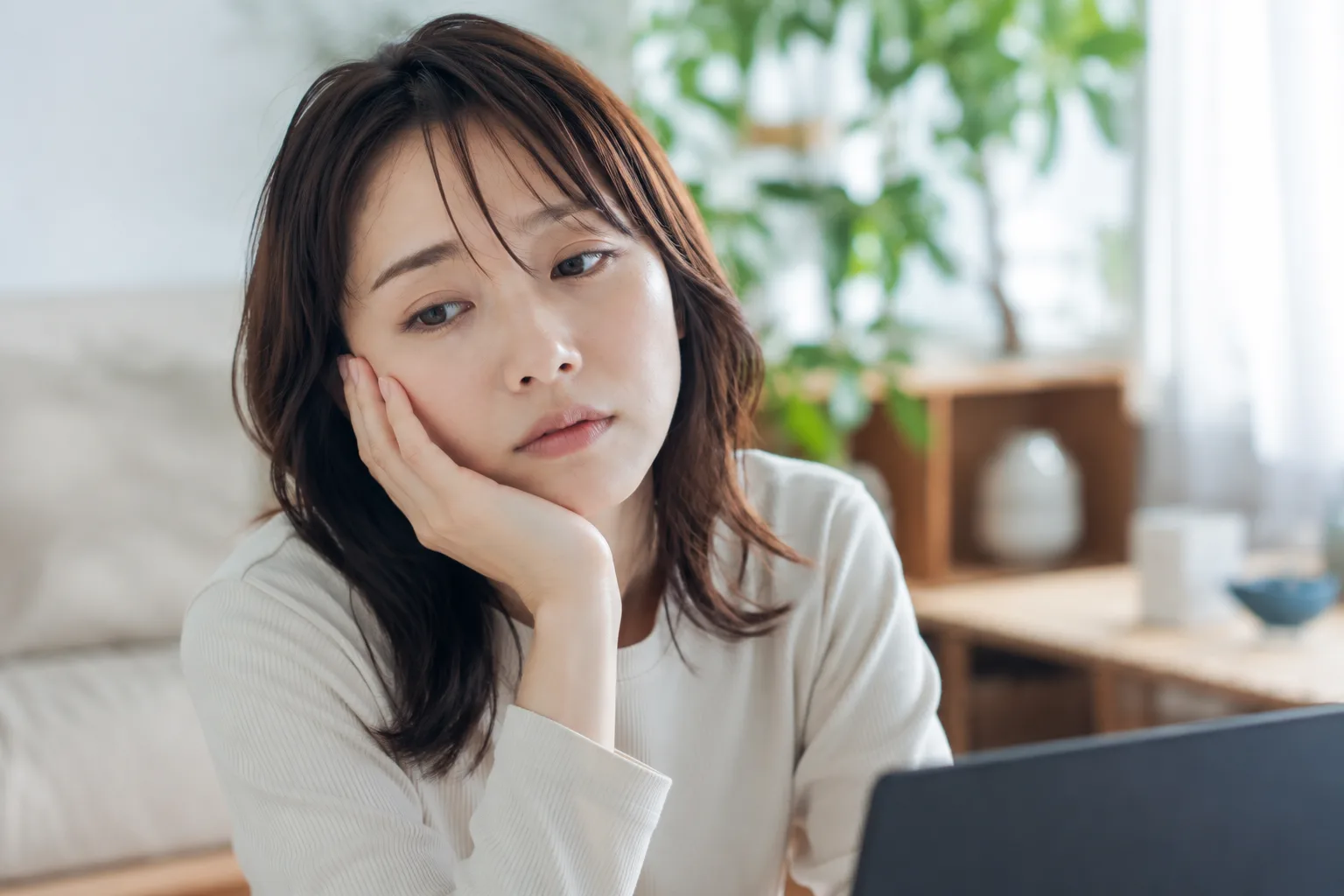 リビングでノートパソコンの画面を見ながら、脱毛の費用や口コミを比較検討し考え込む女性