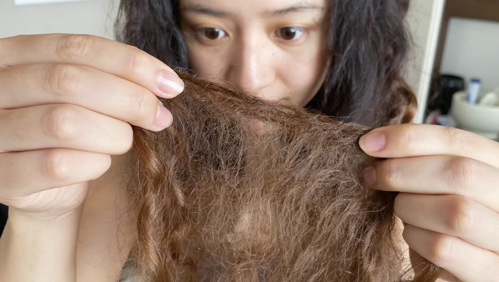 広がってうねった毛束を両手で持ち上げ、髪の状態を間近で確認する女性