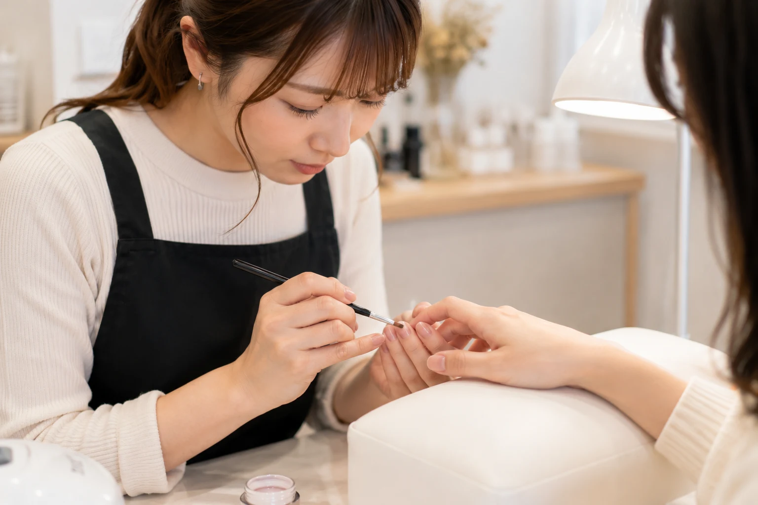 ネイルサロンでネイリストが顧客の爪にジェルネイルを丁寧に施術している様子