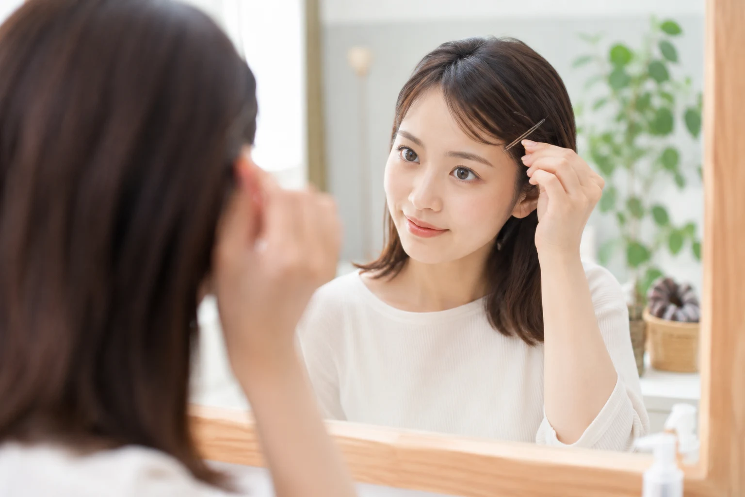 眉上の前髪をヘアピンで留め、伸びた前髪の状態を鏡で確認する女性