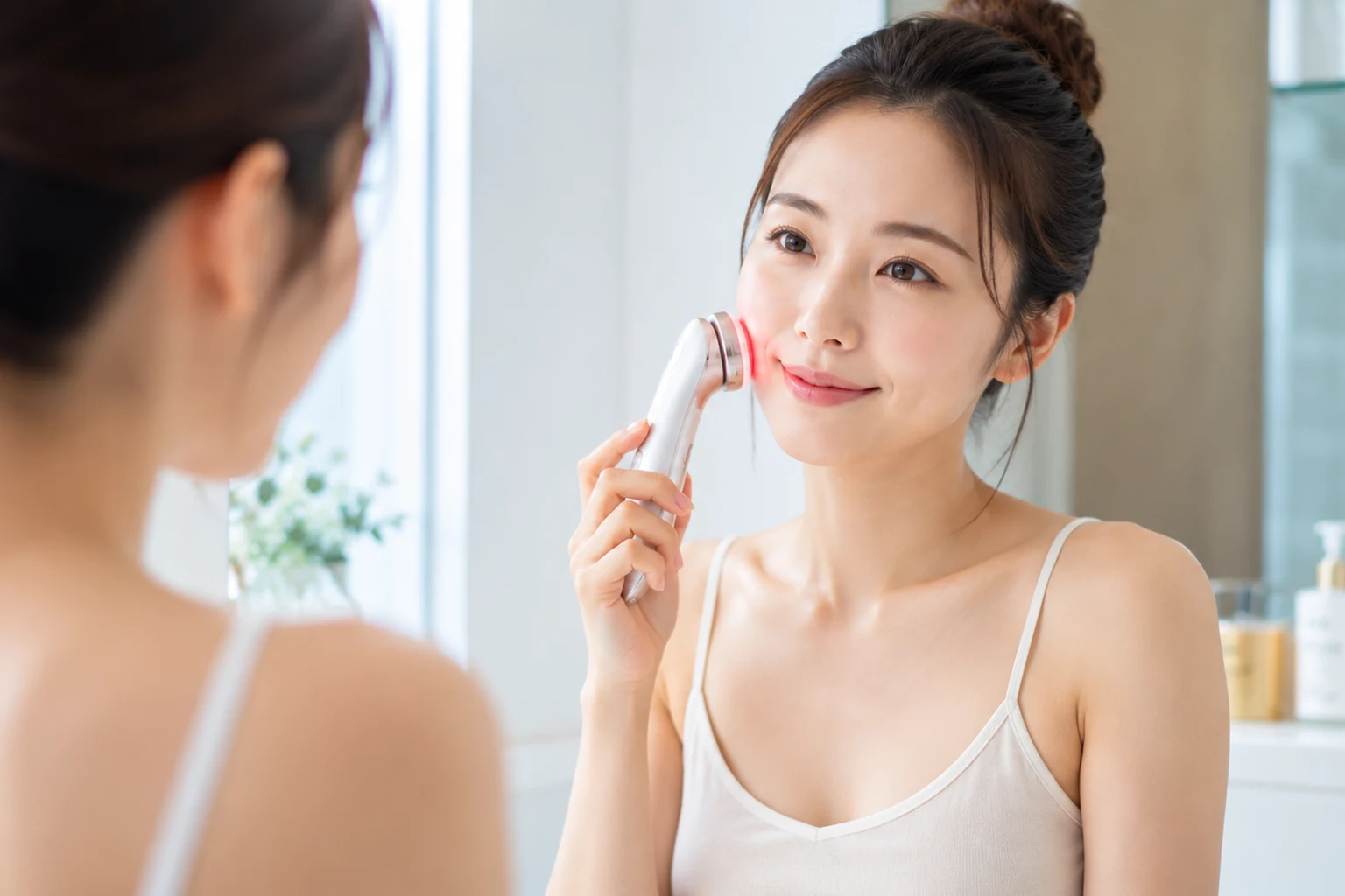 美顔器のヘッドを頬に当ててスキンケアをする女性(肌にほんのり赤みが見える施術中の様子)