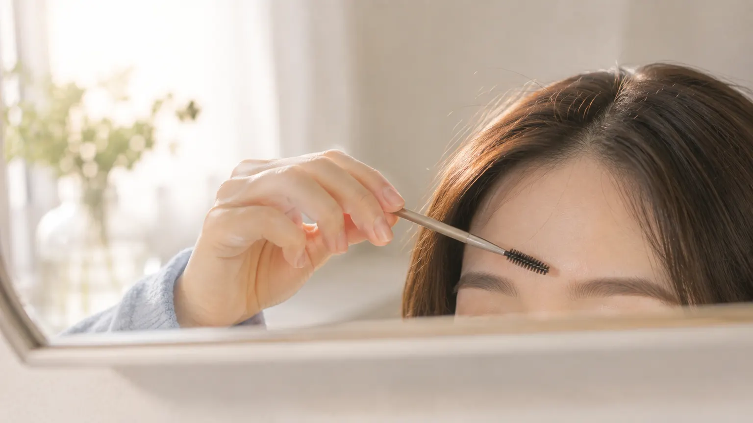 鏡越しにスクリューブラシで眉を整える手元