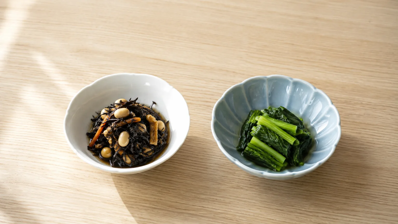 木のテーブルに並べた、ひじきの煮物と青菜のおひたしの2つの小鉢