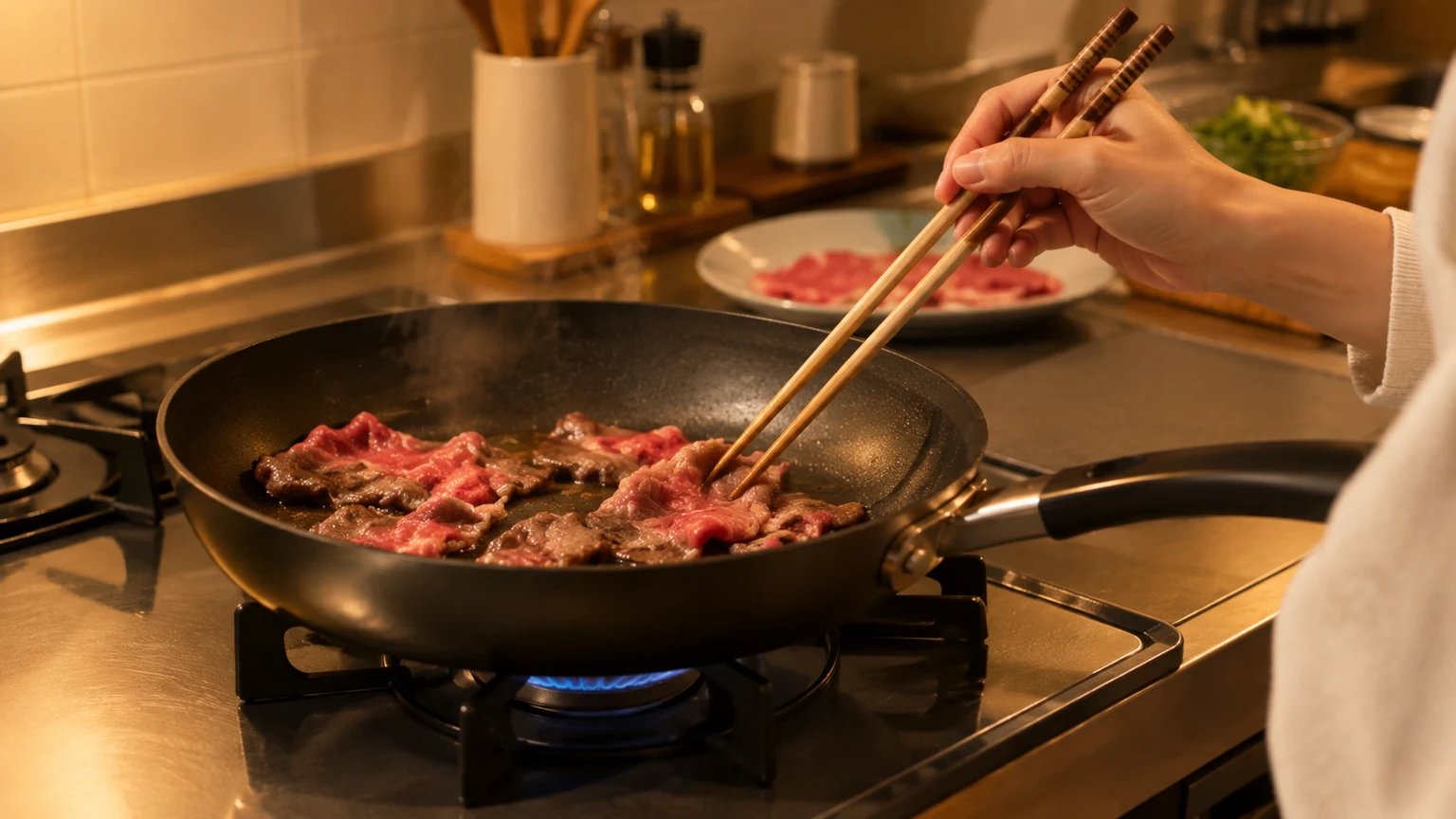 コンロの上のフライパンで、牛肉の赤身の薄切りを菜箸で焼いている手元