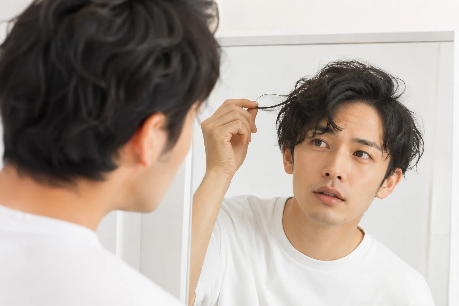 鏡の前で寝ぐせのついた髪を指でつまむ様子